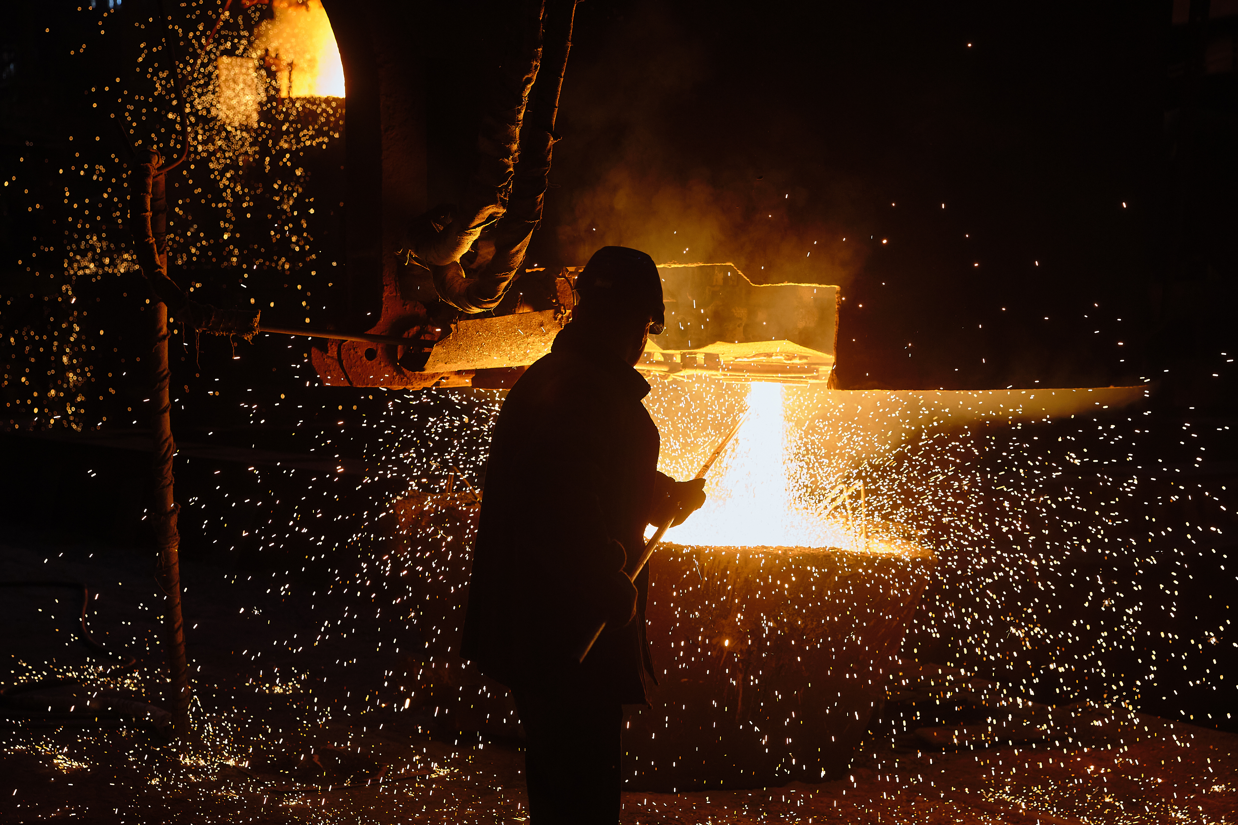 A sample of liquid metal is taken from a ladle by a metal worker. 